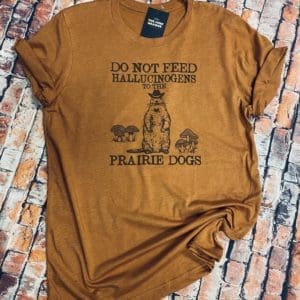 Full view of the do not feed hallucinogens to the prairie dogs t-shirt design with a prairie dog wearing a cowboy hat by sets of mushrooms