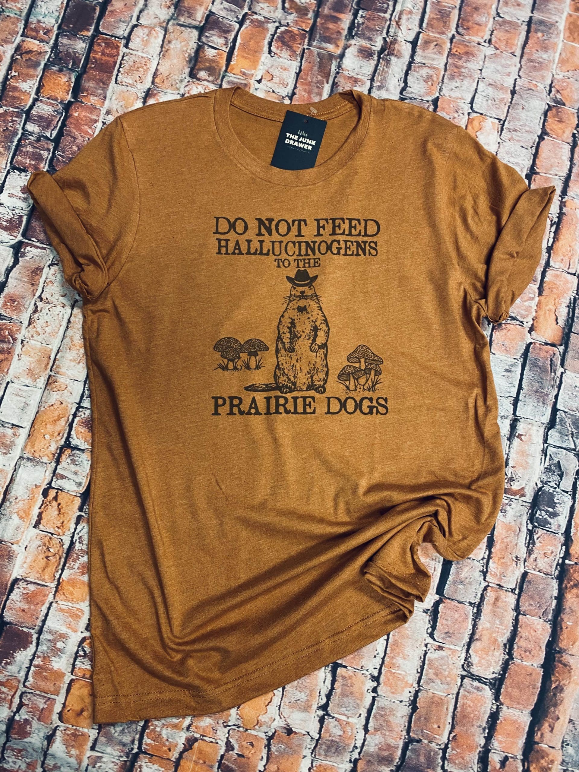 Full view of the do not feed hallucinogens to the prairie dogs t-shirt design with a prairie dog wearing a cowboy hat by sets of mushrooms