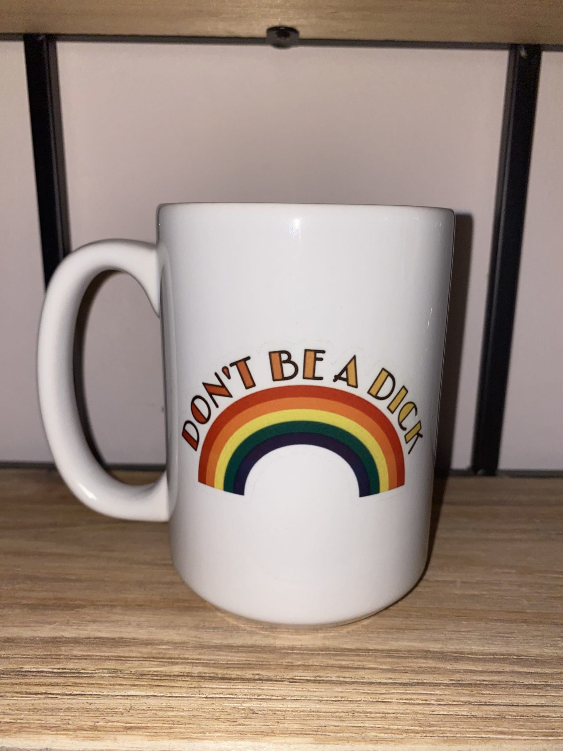 DON’T BE A DICK text with red to yellow gradient above a rainbow custom mug